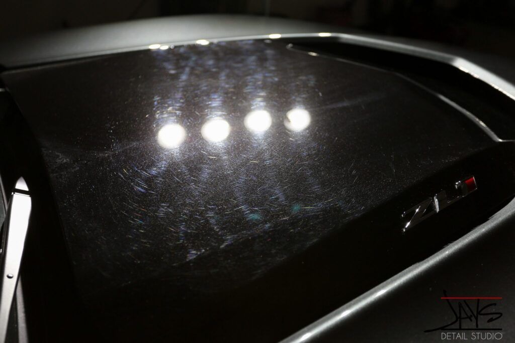 Black car hood with swirls reflecting bright lights.