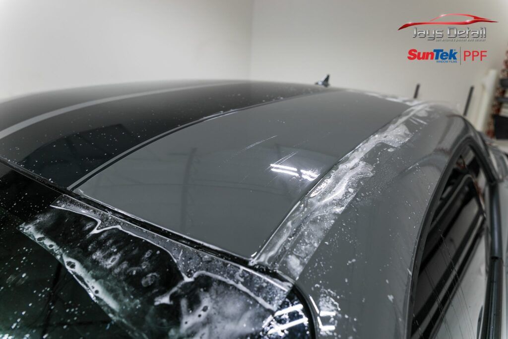 Car roof with wet, protective film being applied, gray stripes visible.