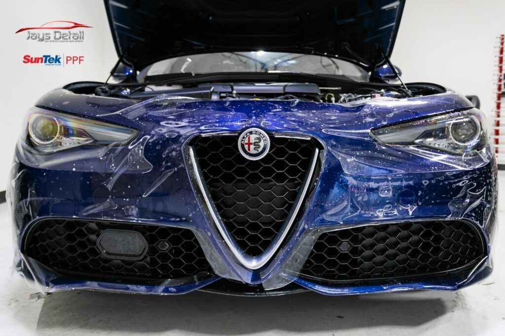 Blue Alfa Romeo car with its hood open, showing a black grill, in a well-lit setting.