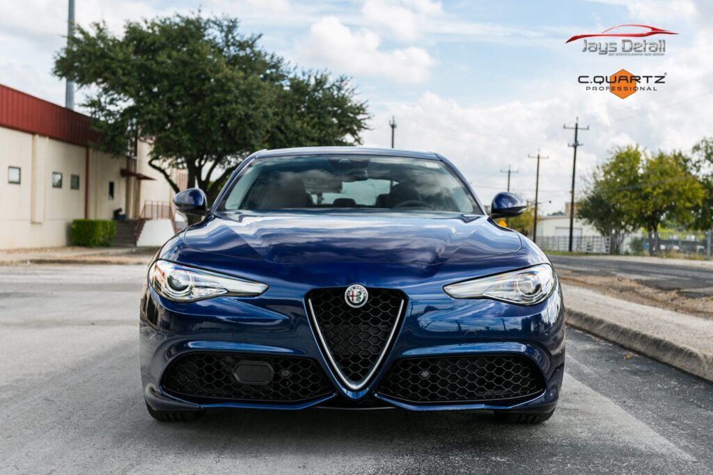 Blue Alfa Romeo Giulia parked on a road, front view, in front of a building and a tree.