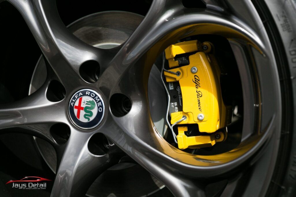 Close-up of a silver car wheel with a yellow Alfa Romeo brake caliper.