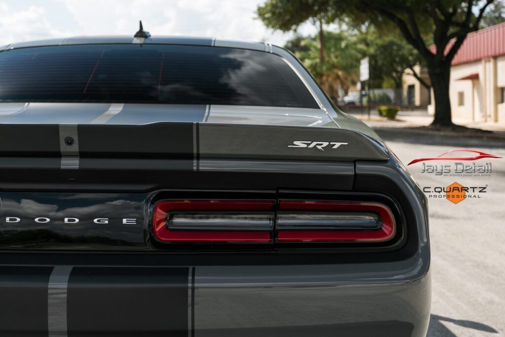 Rear view of a gray Dodge Challenger SRT with racing stripes; taillights illuminated.