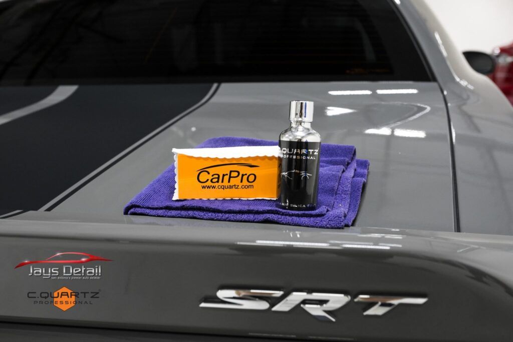 CarPro detailing products on a gray car's trunk, including a bottle, microfiber towel, and applicator pad near the SRT emblem.
