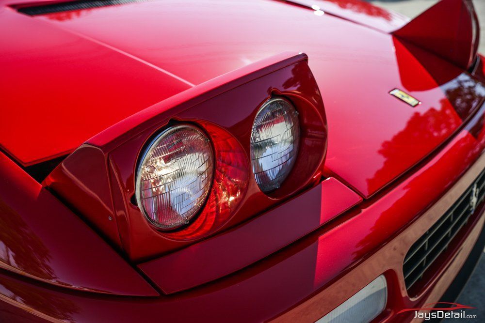 Red Ferrari's pop-up headlights, close up. Shiny red paint, bright sunlight.