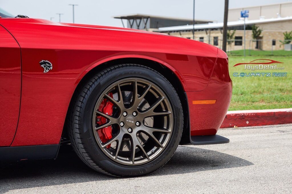 Red Dodge Challenger front quarter panel with a bronze wheel, black tire, and red brake calipers.