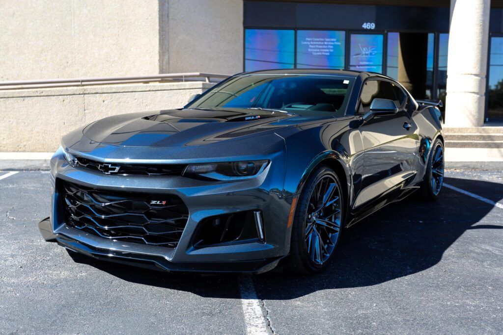 Dark gray Chevrolet Camaro parked in front of a building with a blue sign.