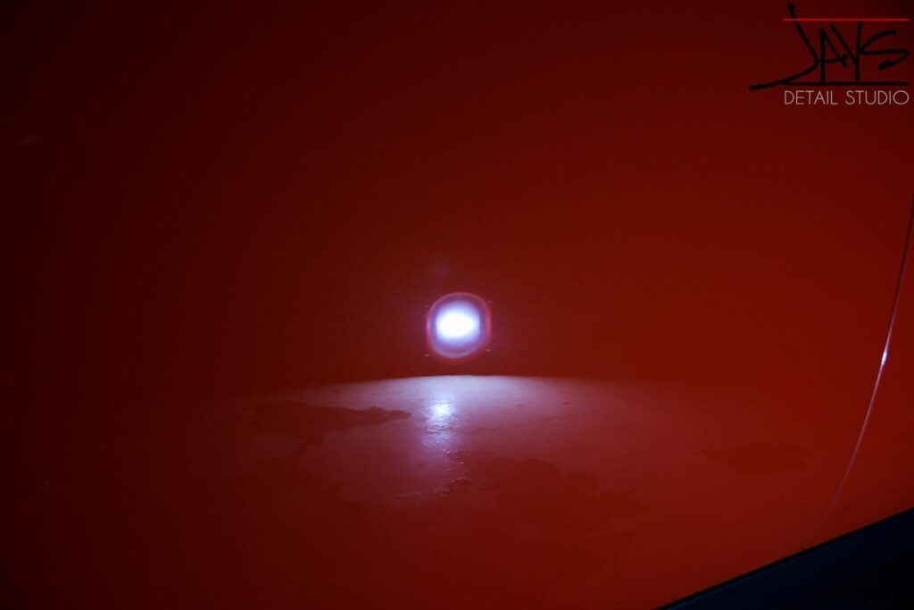 A close-up of a shiny red car surface reflecting a bright overhead light.