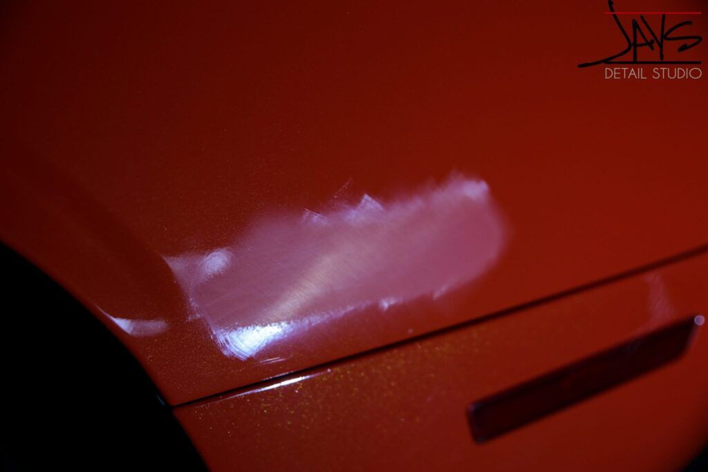 White, hazy damage on a red car's body panel.