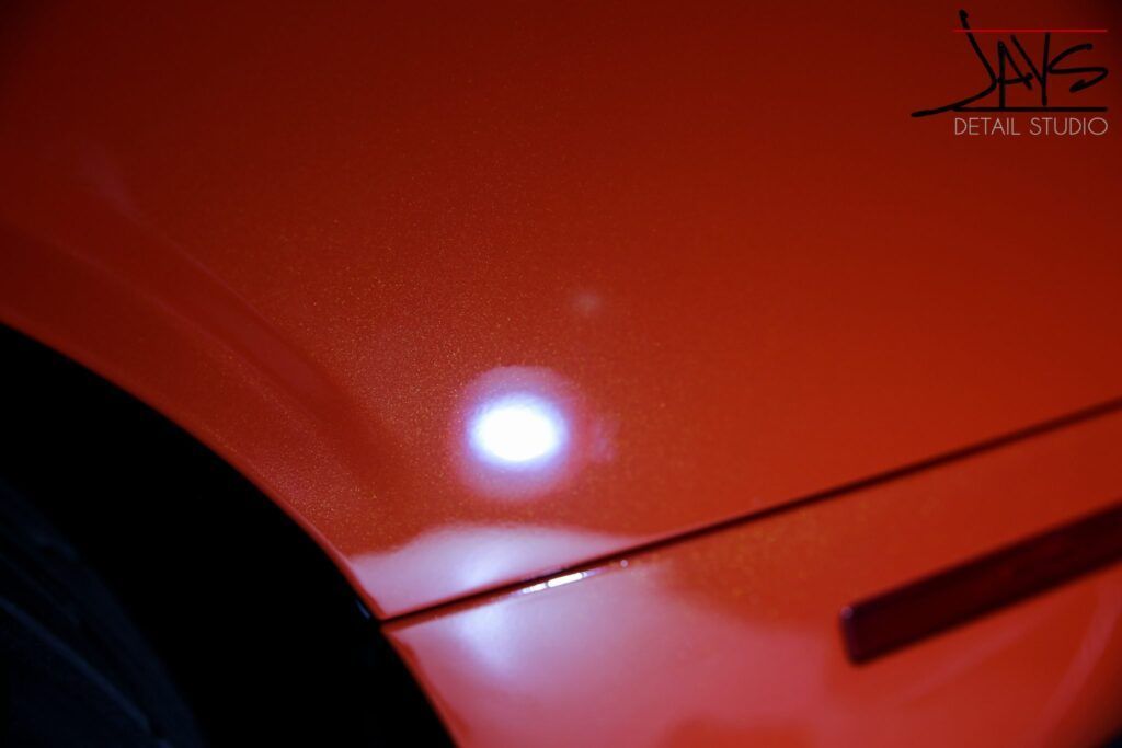 Close-up of a shiny red car fender with a bright light reflecting on it.