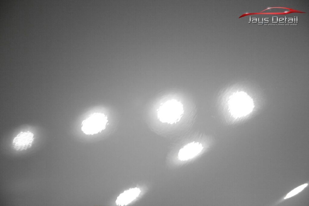 Bright light reflections on a gray surface, possibly polished car paint.