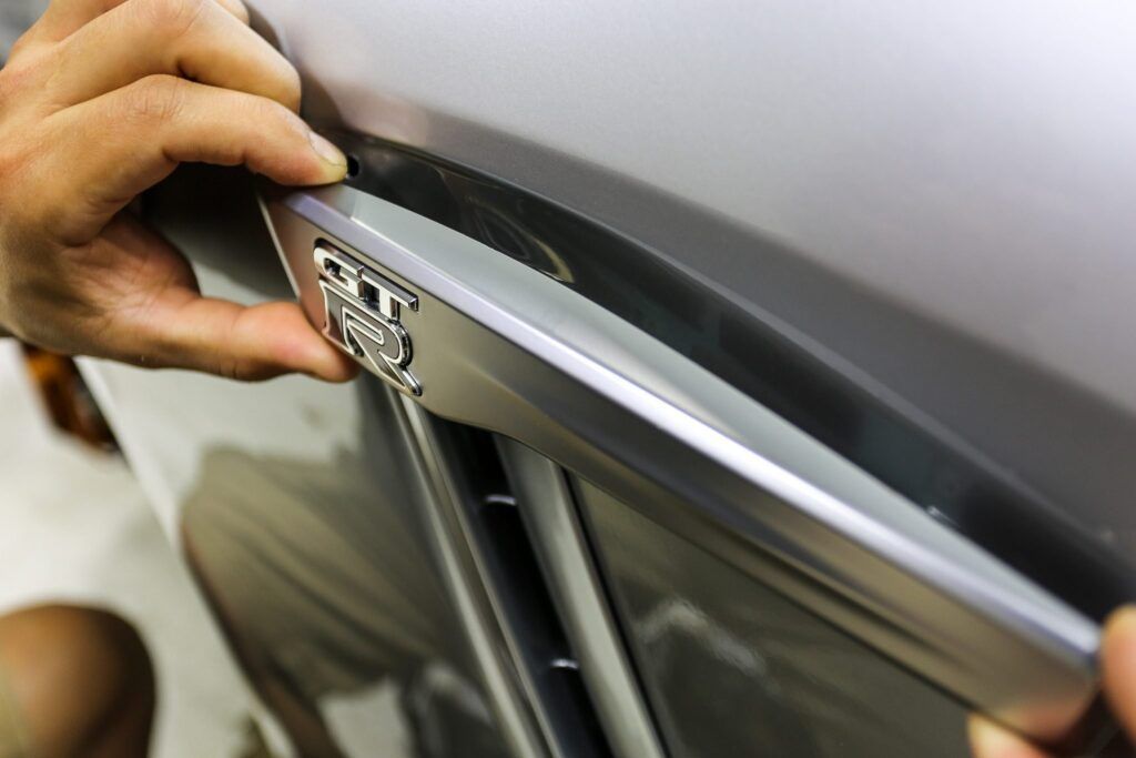 Hands installing a silver car vent trim piece on a gray vehicle.