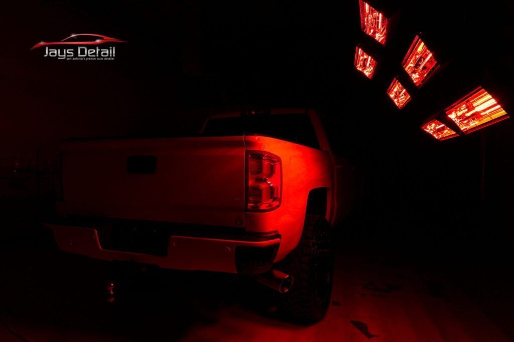 Red-lit truck under infrared lamps in a detailing bay, showcasing the vehicle's rear.