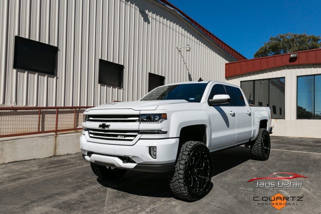 White Chevrolet pickup truck with black wheels parked in front of a building on a sunny day.