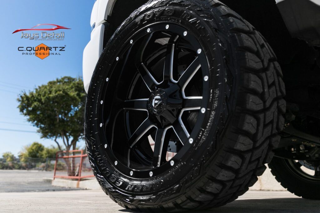 Close-up of a black and silver truck wheel with a rugged tire on a sunny day.