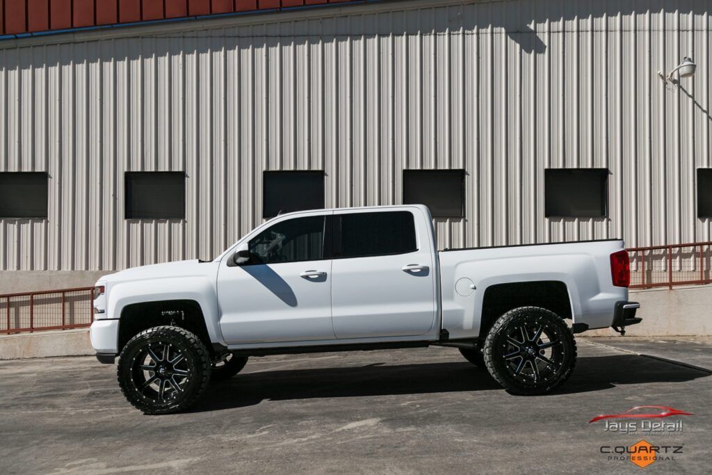 White lifted pickup truck with black rims parked in front of a building.