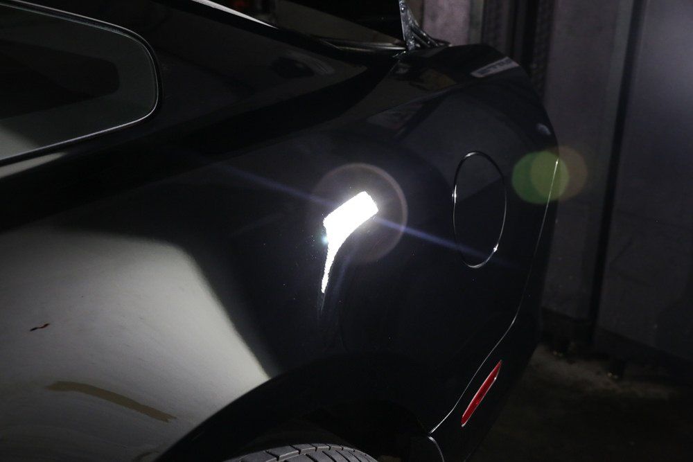 Black car's rear, lit by a bright light reflecting off the body, fuel door visible.