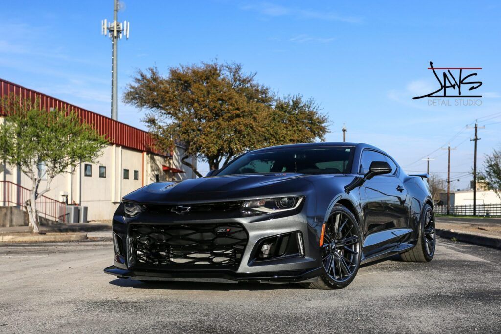 Gray Chevrolet Camaro sports car parked outdoors with a tree and buildings in the background.