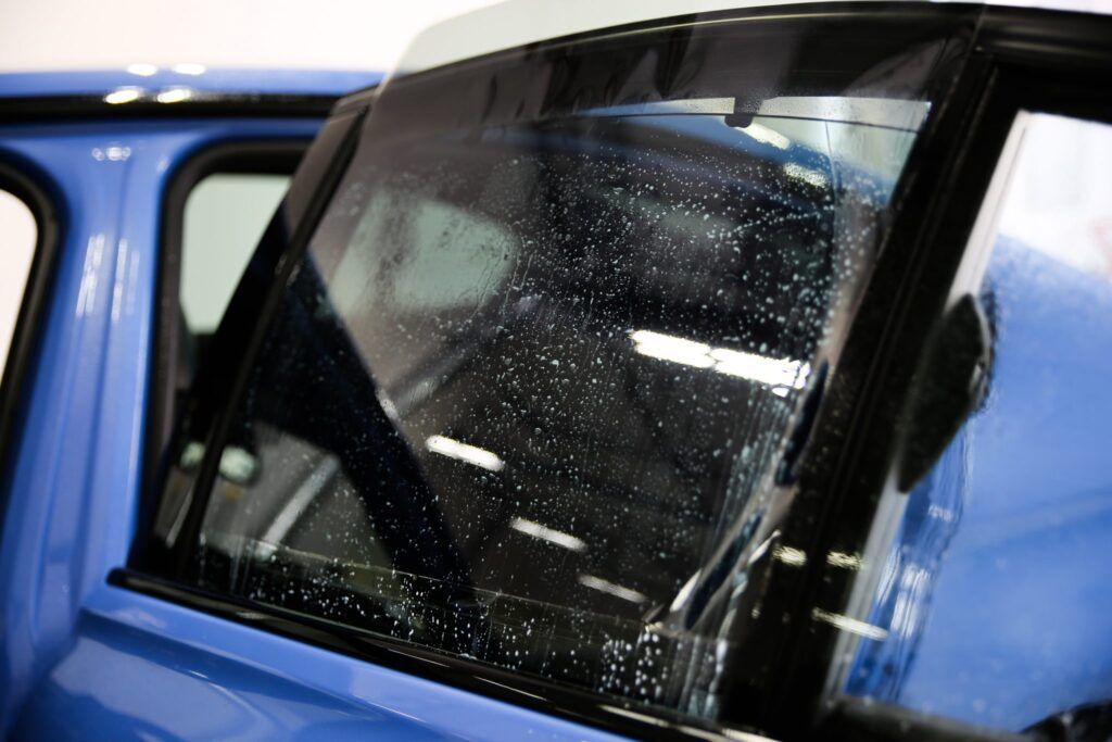 Blue car window being tinted; film applied, showing water droplets.