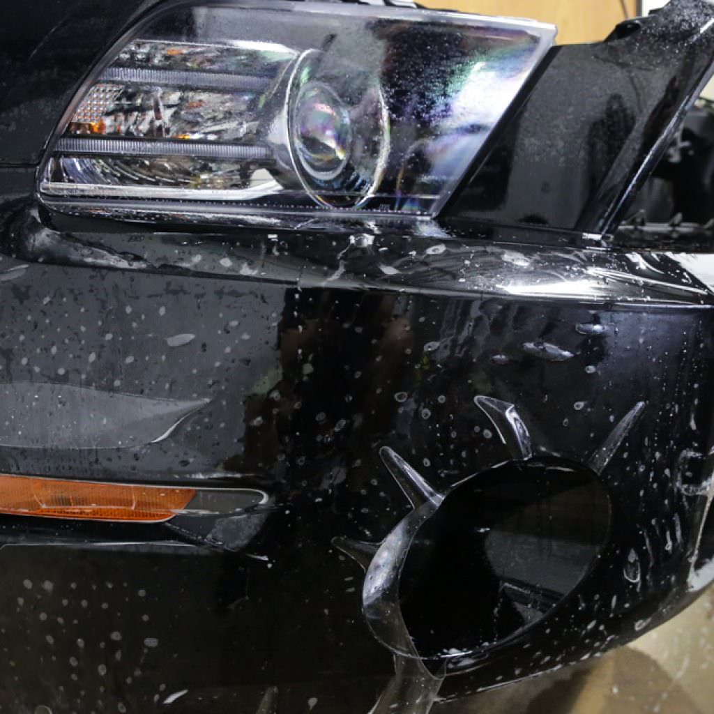 Black car bumper with protective film being applied, next to headlight.