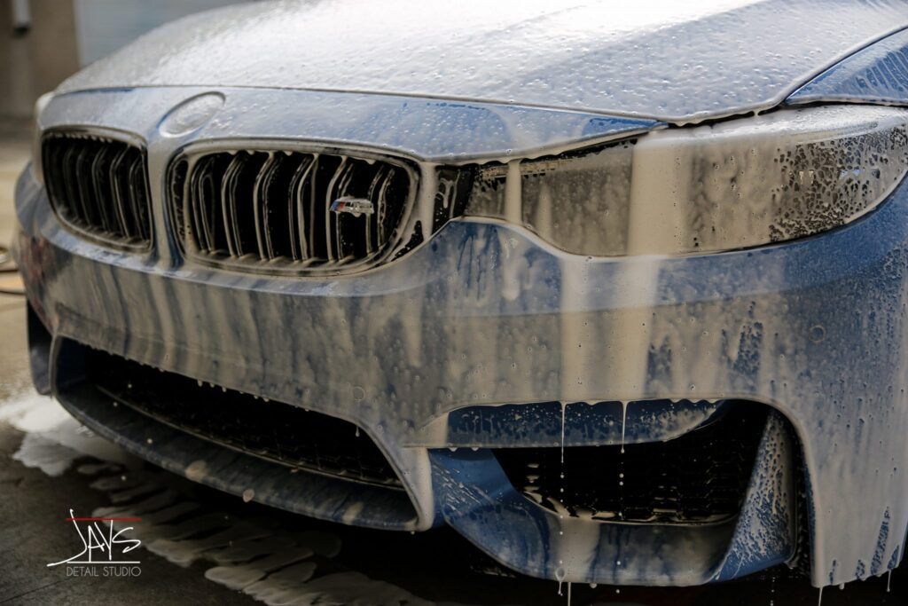 Blue BMW car covered in white soap suds during a car wash.