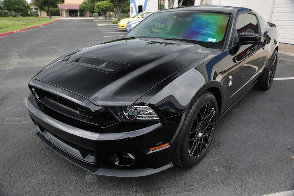 Black Shelby Mustang coupe parked on asphalt.