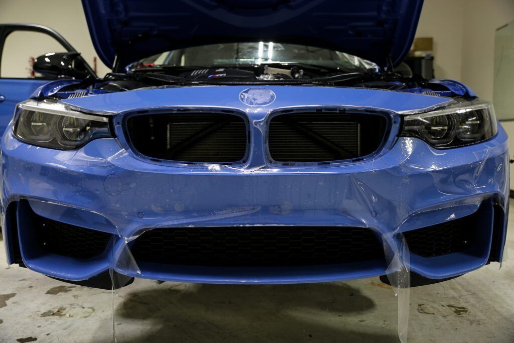 Blue BMW car front with protective film applied, hood open.
