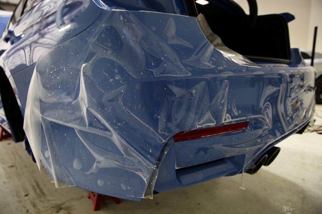 Blue car bumper with clear protective film being applied.