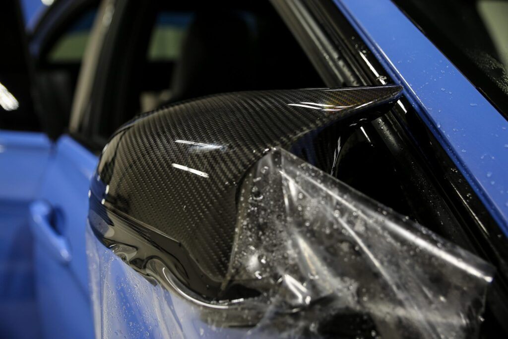 Carbon fiber car side mirror with protective film being applied.