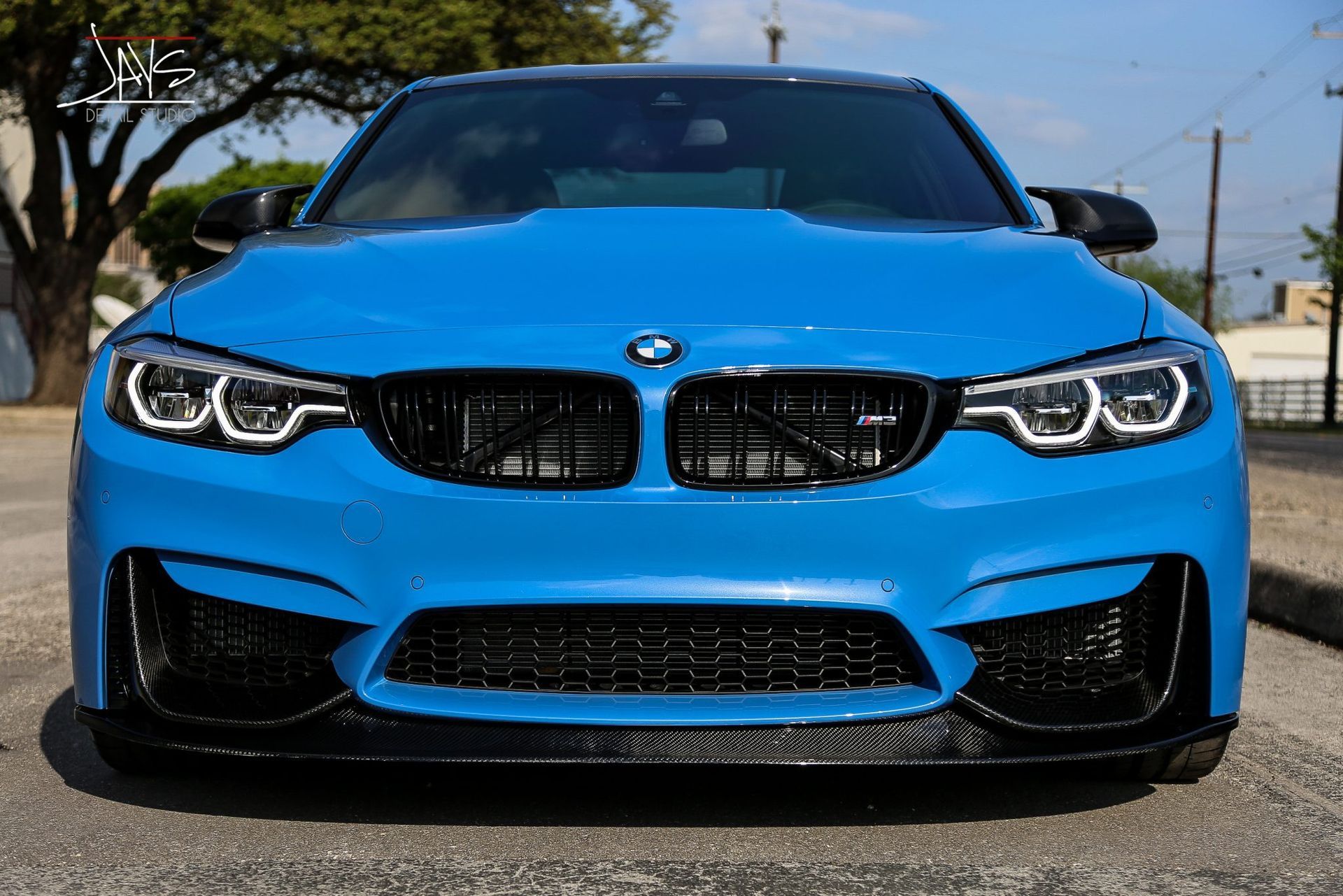 Blue BMW M3 sports car with black accents, parked on a street.