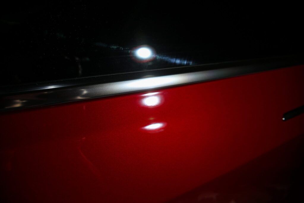 Red car door reflecting bright light against a black background.