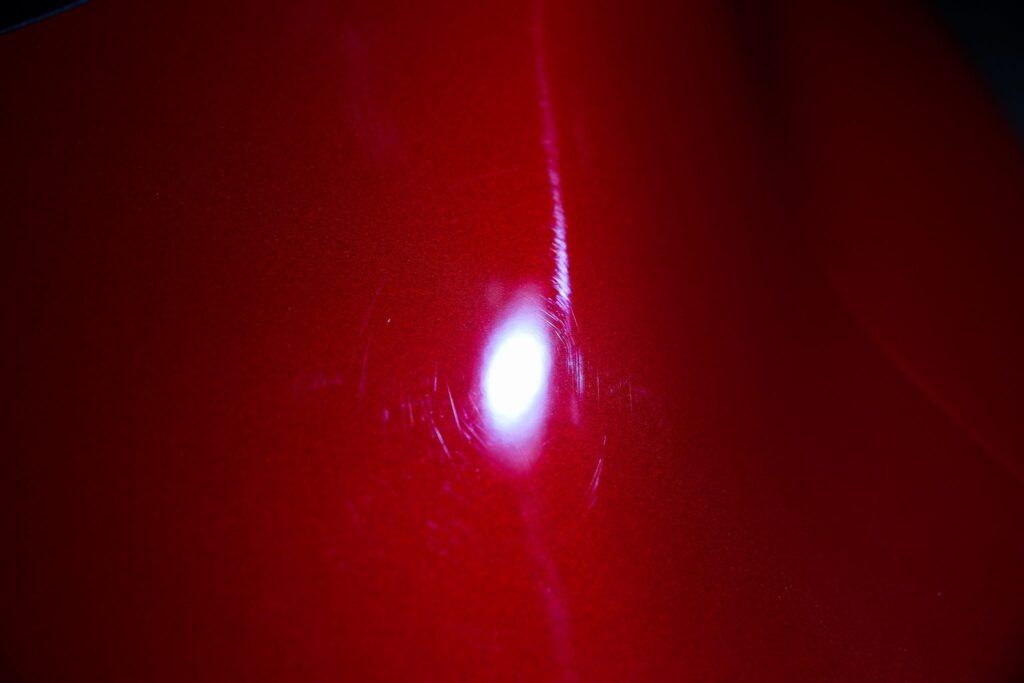 Bright light reflecting on a red surface, showing scratches and imperfections.