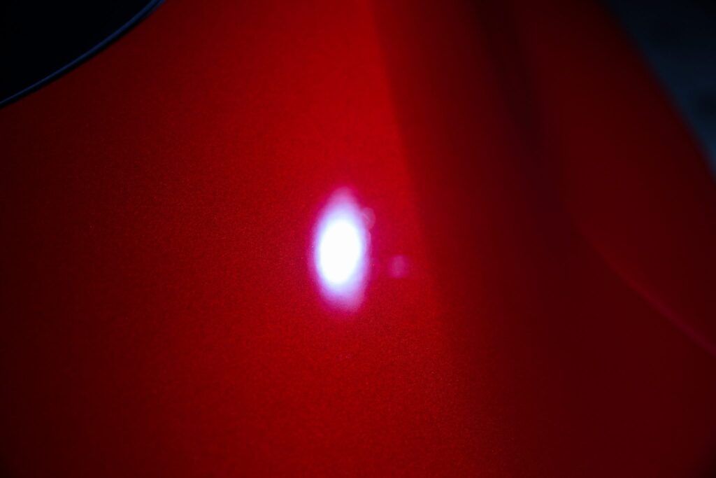 Close-up of a vibrant red car surface with a bright, white reflection.