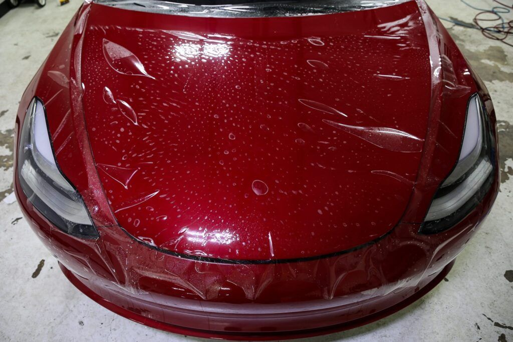 Red car hood with protective film being applied, close-up.