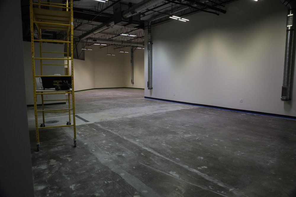 Empty warehouse space with white walls, gray concrete floor, and a yellow scaffolding.