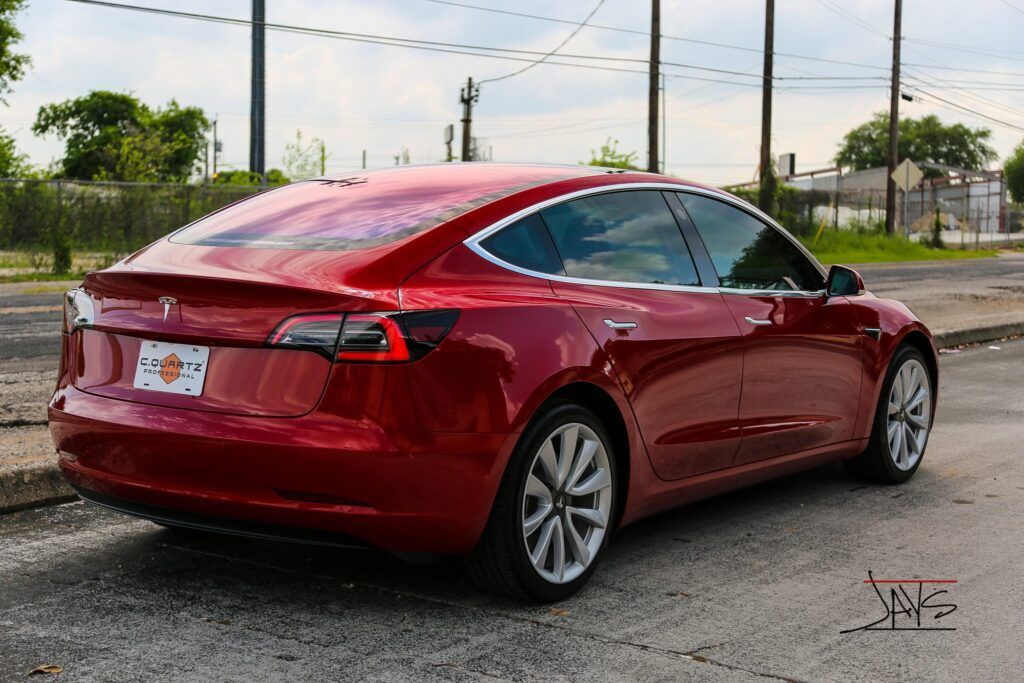 Red Tesla car parked on a street with a city background.