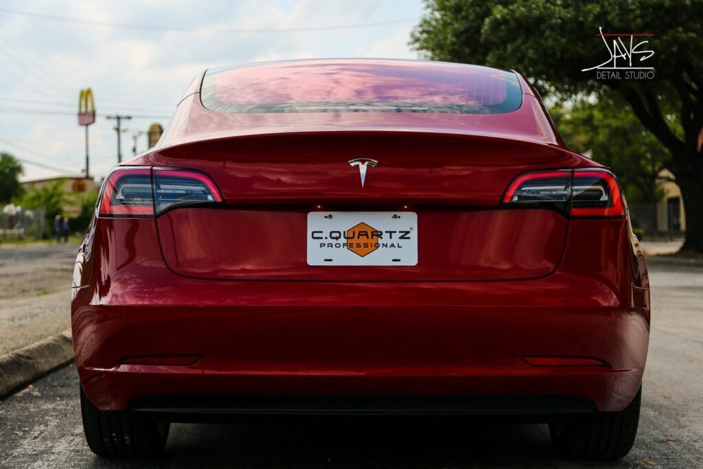 Red Tesla car's rear view with a license plate. A McDonald's sign and tree in the background.