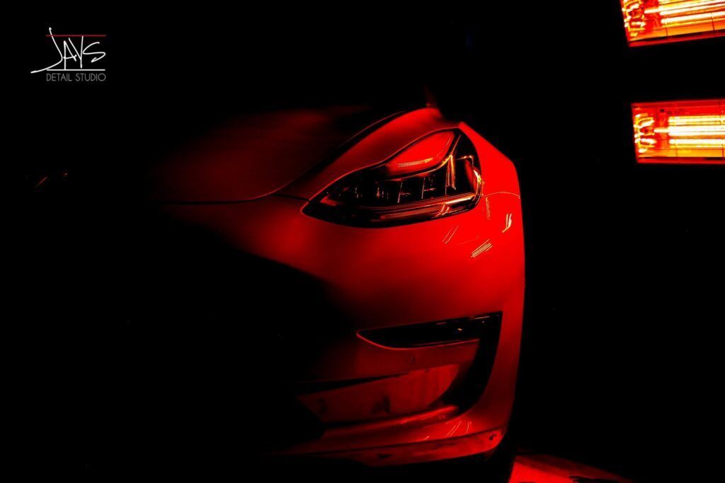Red Tesla car front lit with red lights in the dark.
