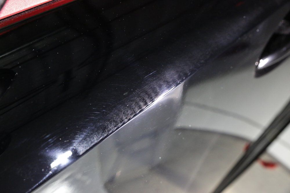 Black car's rear edge with scratches and faded paint, likely damaged by sun or wear and tear.