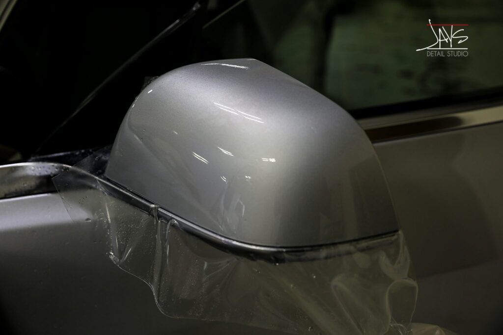 Close-up of a silver car side mirror covered in plastic wrap.