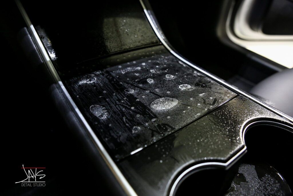 Black Tesla Model 3 console, showing a faded pattern on the surface, with cupholders visible.