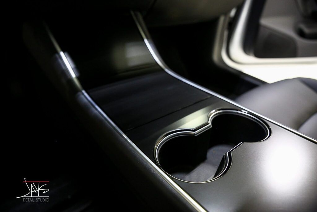 Close-up of a Tesla car's center console with cup holders, sleek black surfaces, and chrome trim.