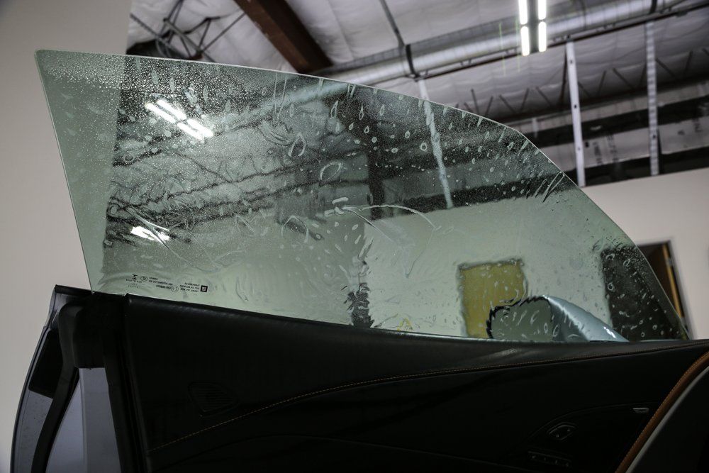 Car window with tinted film being applied. The car is black, in a shop setting.