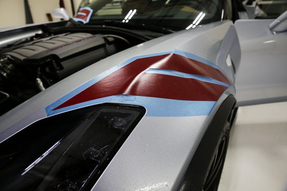 Silver car fender with red and blue tape, likely for painting a design.