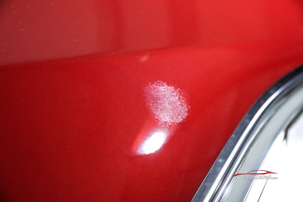 Close-up of red car paint with a cluster of white, damaged paint.