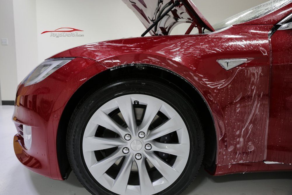 Red Tesla being fitted with clear paint protection film.