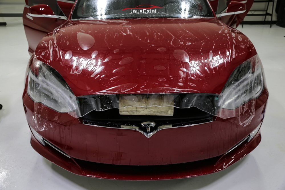 Red Tesla car with clear protective film being applied to the front bumper and hood.