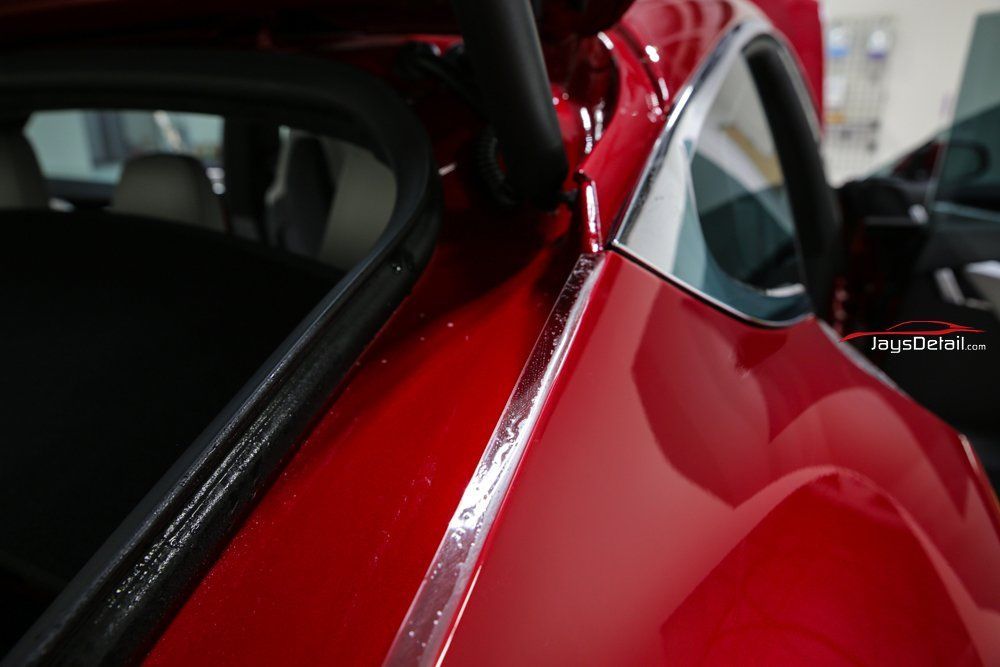 Red car rear panel with chrome trim and black rubber seal.