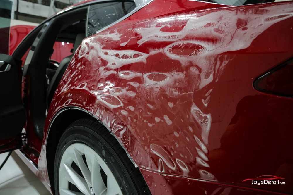 Red car with soap suds on the rear quarter panel during detailing.