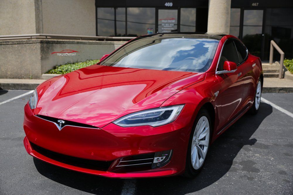 Red Tesla Model S parked outside a building with tinted windows.