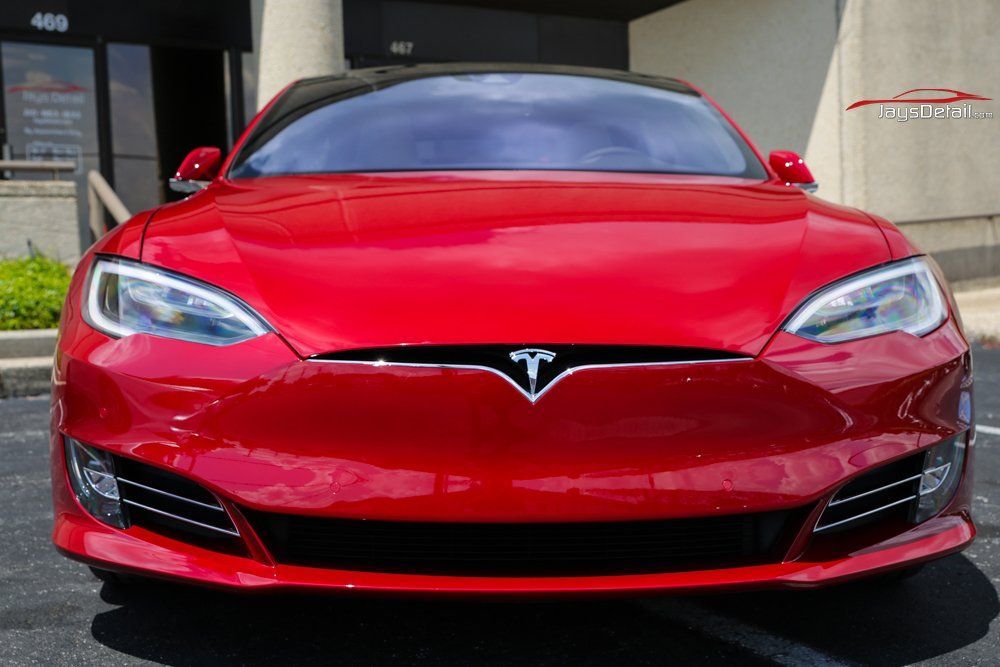 Red Tesla Model S parked in front of a building, facing forward.